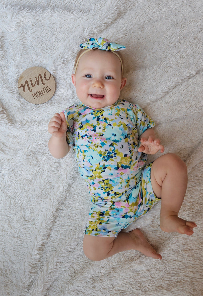 Baby in a floral lounge set on a textured surface with a 'nine months' milestone card.