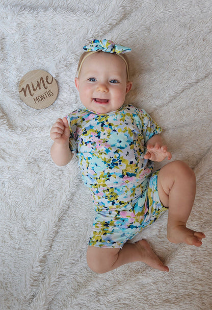 Baby in a floral lounge set on a textured surface with a 'nine months' milestone card.